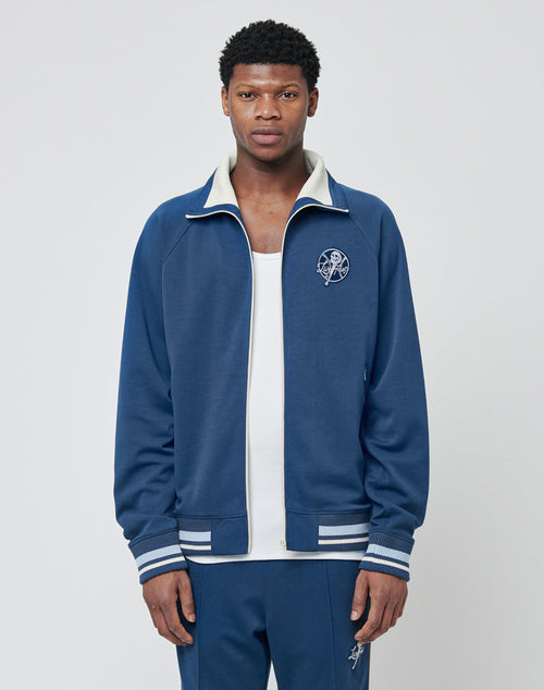 A man faces forward wearing a LIVE FAST DIE YOUNG Track Suit Jacket with white trim and a circular logo on the left chest, paired with matching blue pants against a plain, light background.