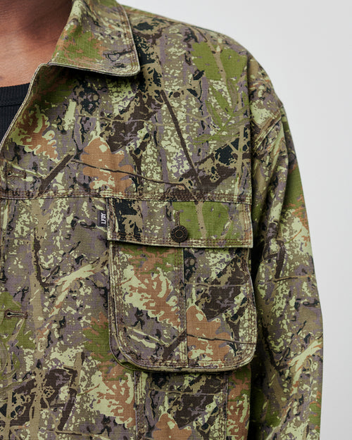 Close-up of the LFDY Hunter Jacket by LIVE FAST DIE YOUNG in a rugged camo pattern. Made from 100% Baumwolle, it features a buttoned front pocket and collar, worn over a black shirt. Only part of the upper chest and shoulder in Regular Fit is visible.