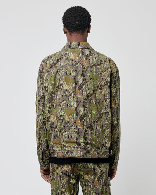 A person stands facing away from the camera, wearing a LIVE FAST DIE YOUNG LFDY Hunter Jacket and matching 100% Baumwolle pants in a green and brown camouflage pattern, set against a plain light background.