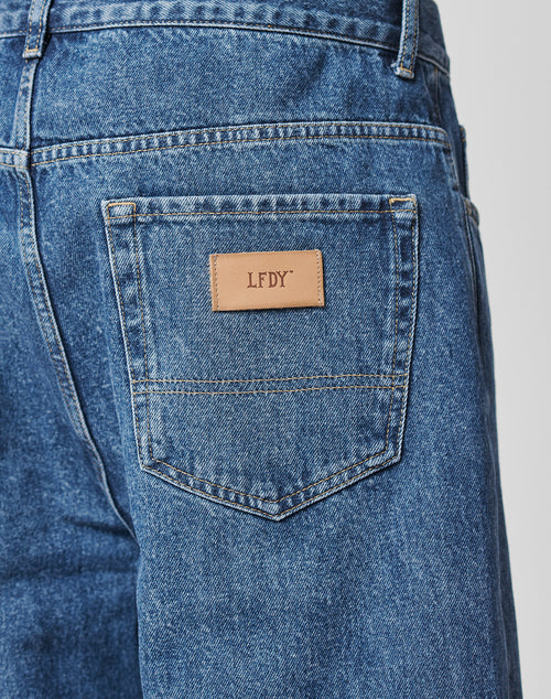 Close-up of the back pocket of LFDY Wide Denim jeans, showing a rectangular tan leather patch embossed with "LFDY." Style LF2103-11721, made from 100% cotton for comfort and durability.