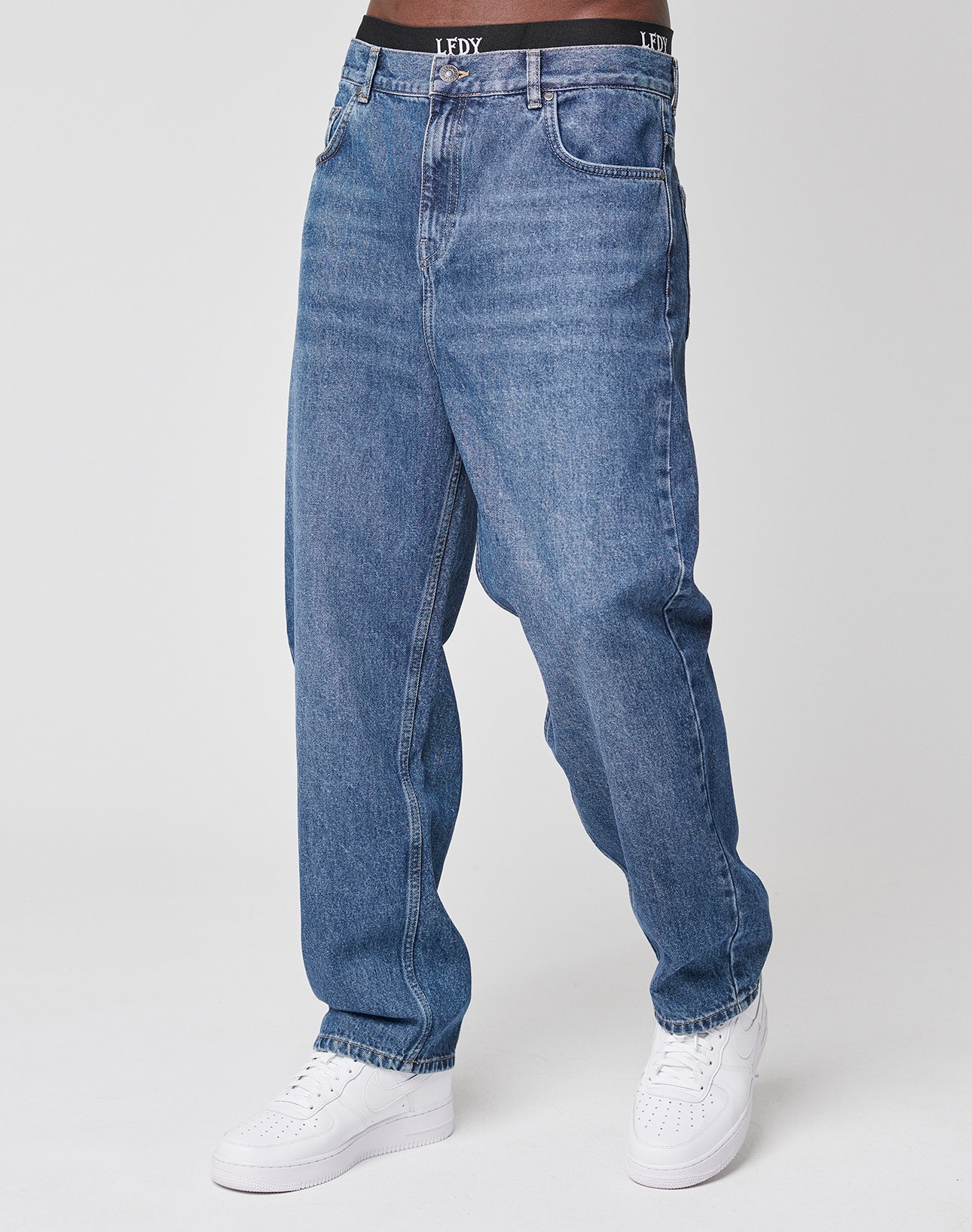 A person in loose-fitting LFDY Wide Denim jeans, white sneakers, and black LFDY underwear (LF2103-11721) stands against a plain light background. Only the lower half of their body is visible.
