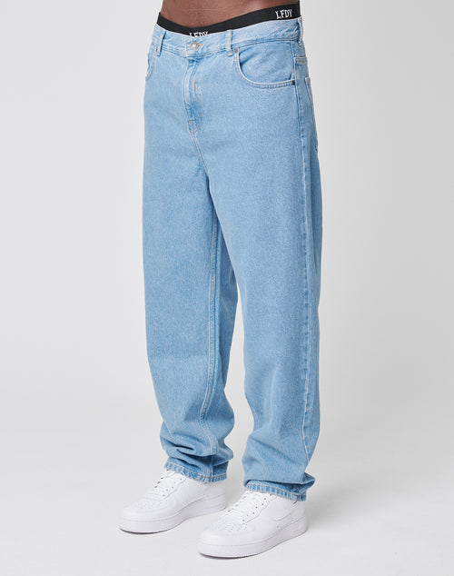 A person wearing LFDY Wide Denim in light blue cotton, paired with white sneakers. The black underwear waistband is visible above the true to size jeans. Shown from chest down against a plain white background.