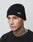A person wearing the black LFDY Beanie with the white LFDY logo, a regular fit black shirt, hoop earring, and visible neck and face tattoos stands against a plain light gray background.