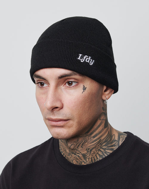 A person wearing the black LFDY Beanie with the white LFDY logo, a regular fit black shirt, hoop earring, and visible neck and face tattoos stands against a plain light gray background.