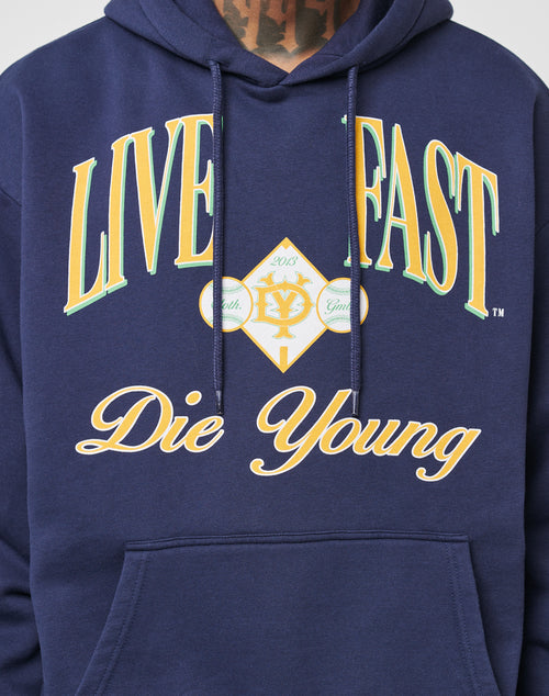 A person wearing the Live Fast Campus Hooded by LIVE FAST DIE YOUNG: a navy blue oversized hoodie with bold yellow LIVE FAST, cursive Die Young, baseballs, a diamond design, and a trendy vintage effect.