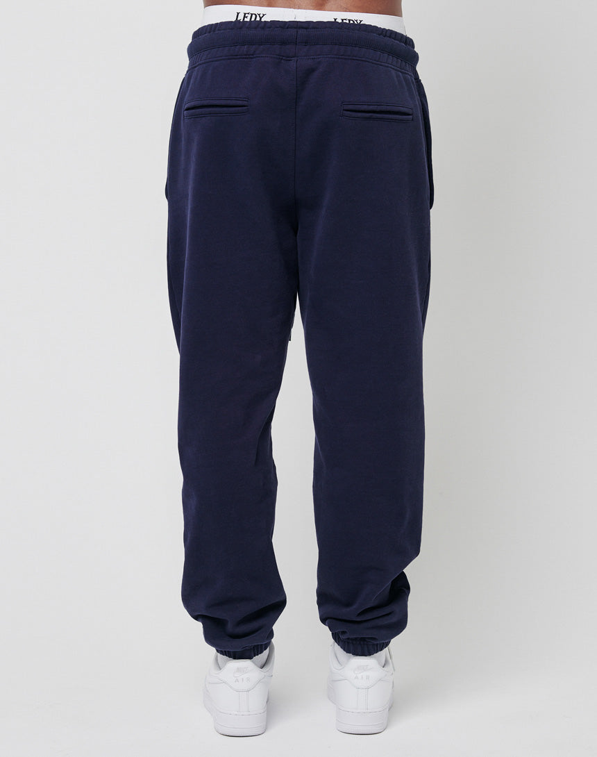 A person wearing LIVE FAST DIE YOUNG's Live Fast Sweat Jogger in Regular Fit navy blue 100% Baumwolle with back pockets and white sneakers, shown from the back against a plain light background.