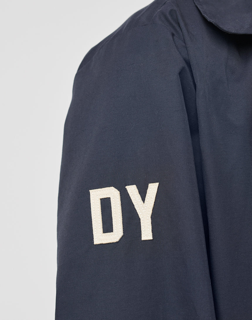 A close-up of the LFDY Trench Coat by LIVE FAST DIE YOUNG features a dark blue sleeve with white "DY" stitching, regular fit, and concealed button placket.