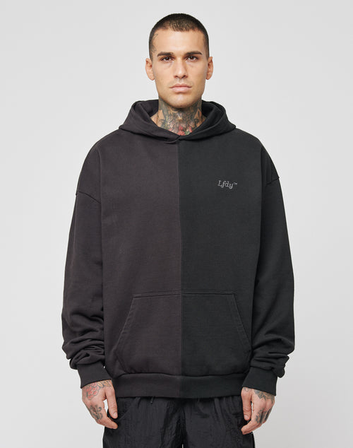 A man with short hair and neck tattoos wears the LFDY Split Hooded, an oversize black two-tone cotton hoodie with a front pocket and subtle logo on the left chest, standing against a light plain background.
