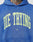 Someone wears the Die Trying Hooded by LIVE FAST DIE YOUNG, a blue oversized hoodie with bold yellow DIE TRYING lettering, small white LFDY text underneath, and a subtle vintage effect; part of a tattooed neck shows above the collar.