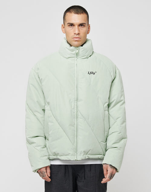 A person wearing a light green LFDY Puffer Jacket with an oversize fit, high collar, and LFDY logo on the left chest stands facing forward against a plain white background.