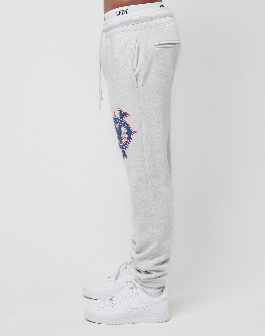 A person in LIVE FAST DIE YOUNG DY Sweat Jogger pants, light gray with blue and orange thigh graphic, regular fit, drawstring waist, pockets, and vintage effect stands sideways. White sneakers finish the look.