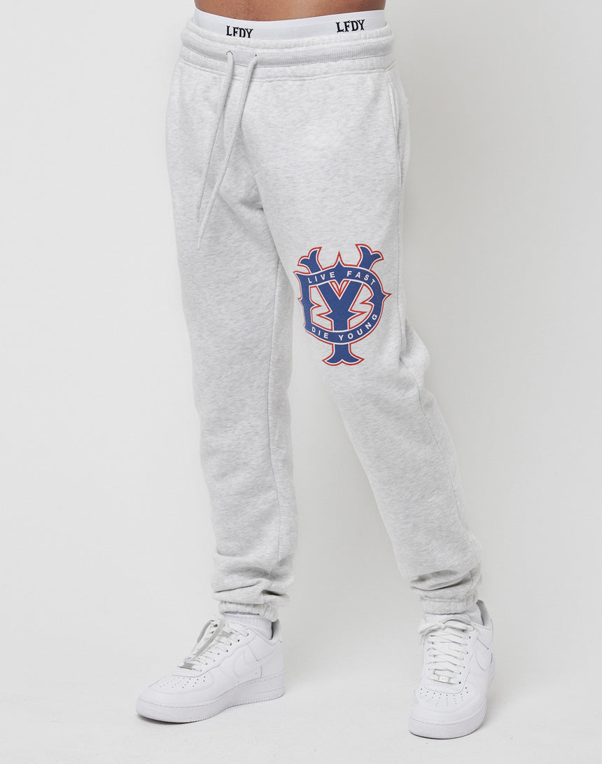 A person wears LIVE FAST DIE YOUNG’s DY Sweat Jogger in light gray with a vibrant graphic and text on the left thigh, LEDY on the waistband, and a regular fit, paired with white sneakers against a plain white background.