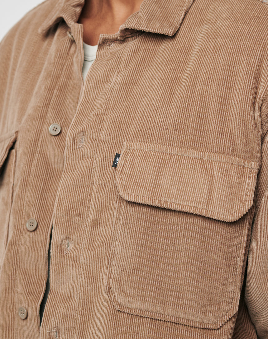 Close-up of a person wearing the LFDY Corduroy Shacket in tan Regular Fit with buttons, front pocket featuring a small fabric tag, and part of a white shirt visible underneath.