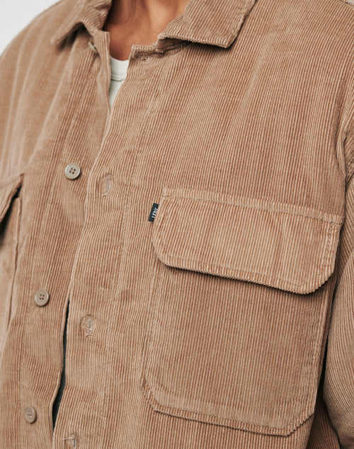Close-up of a person wearing the LFDY Corduroy Shacket in tan Regular Fit with buttons, front pocket featuring a small fabric tag, and part of a white shirt visible underneath.