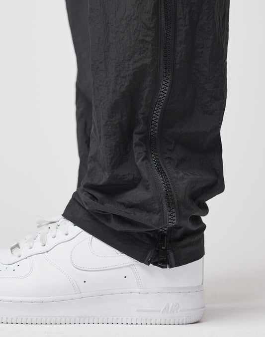 Close-up of a person wearing white Nike Air Force 1 sneakers and black LFDY Zip Tape Track Pants, featuring a vertical ankle zipper.