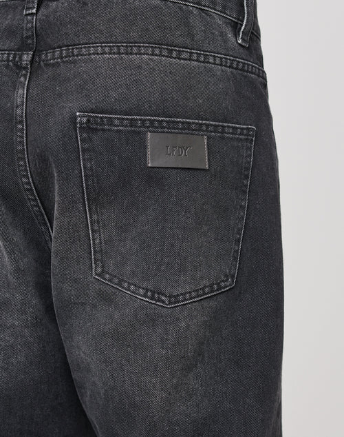 Close-up of the back pocket on LIVE FAST DIE YOUNG Regular Denim jeans. The black 100% cotton denim shows a worn texture, and a rectangular Lederpatch with LFDT is embossed above the pocket.