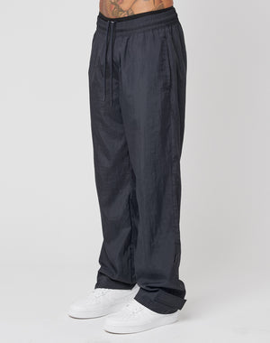A person wears LIVE FAST DIE YOUNG Nylon Jogger track pants in dark gray with a wide elastic waistband and drawstring, paired with white sneakers. The photo is cropped from lower torso to feet.