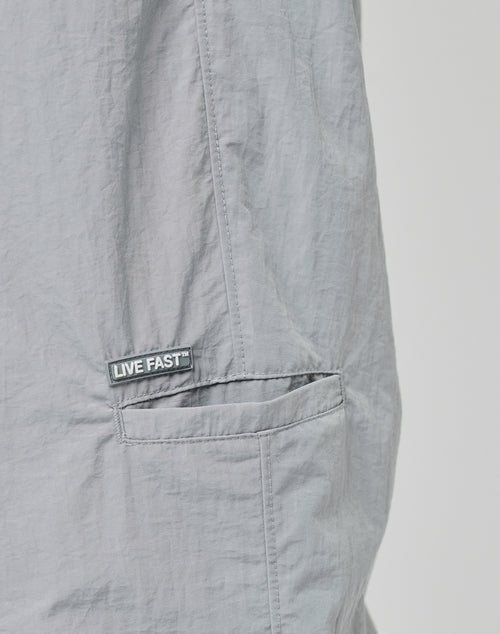 Close-up of light gray wrinkled Nylon on LFDY Calf Zip Pants, featuring a small pocket with an elastic waistband and a black and white LIVE FAST label above it.