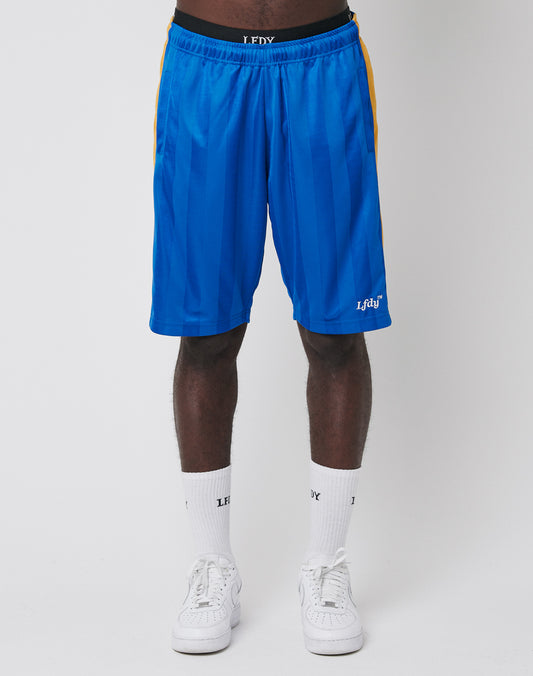 A person wears bright blue LFDY Taped Stripe Shorts with an elastic waistband, yellow side stripes, and LFDY branding at the waistband and left hem, paired with white crew socks and sneakers against a plain white background.
