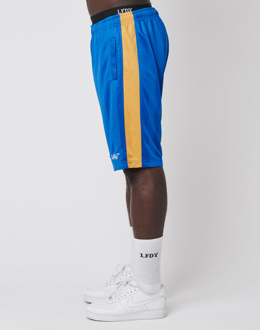 A person stands sideways in LFDY Taped Stripe Shorts with yellow stripe, an elastic waistband, and polyester fabric, paired with white LFDY socks and white sneakers, all set against a plain white background.