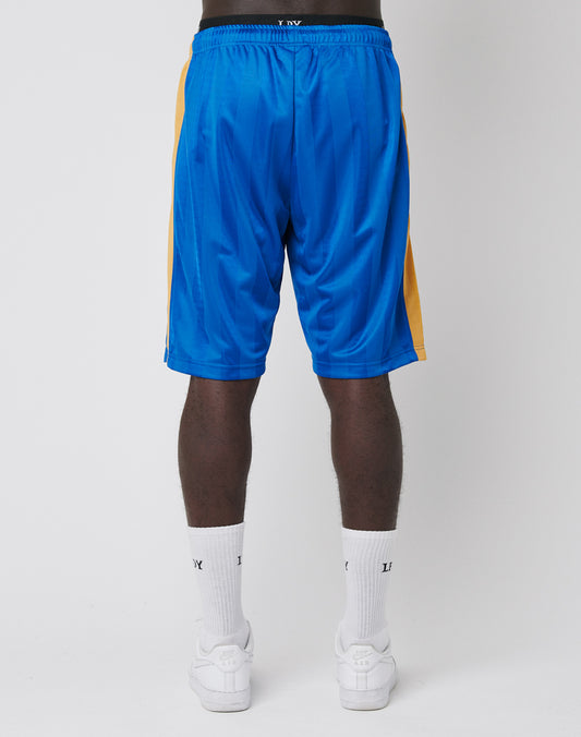 A person stands facing away, wearing blue LFDY Taped Stripe Shorts with yellow side panels, white socks, and white sneakers against a plain white background.
