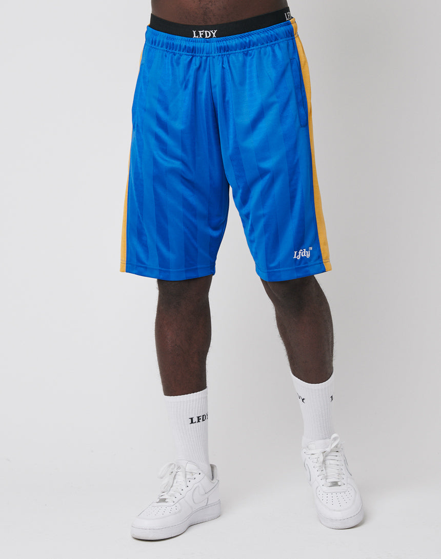 A person wearing LFDY Taped Stripe Shorts—bright blue with yellow stripes, Elastik-Bund, Polyester material, Regular Fit—paired with branded white socks and sneakers stands against a plain white background.
