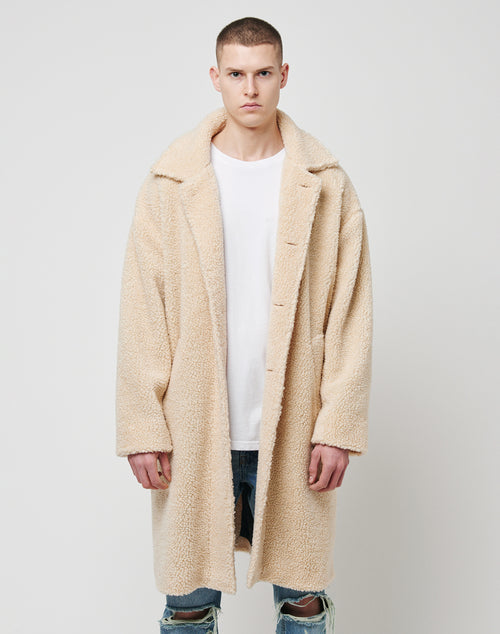 A person stands facing forward, wearing an LFDY Sherpa Coat over a white t-shirt and ripped blue jeans, against a plain light gray background.