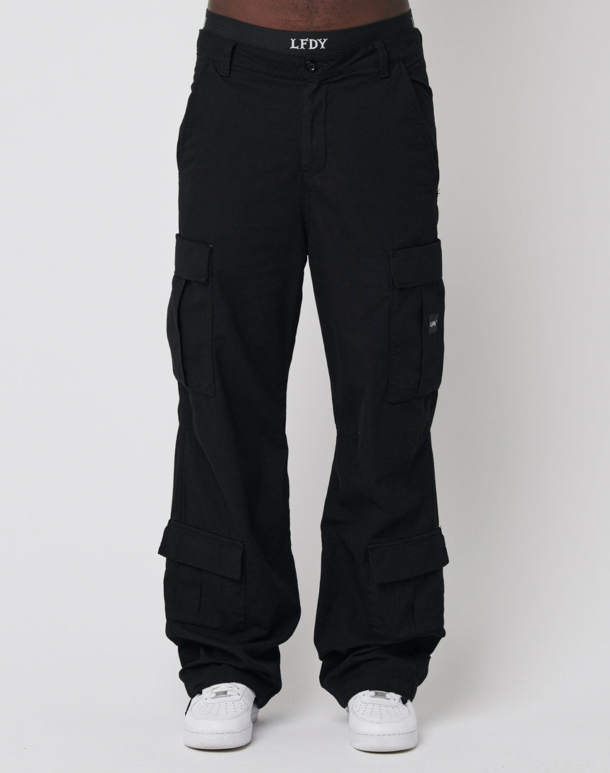 A person wears LFDY’s Wide Summer Cargo—black, wide fit cotton pants with multiple pockets—styled with a branded LFDY belt and white sneakers, standing against a plain light background.