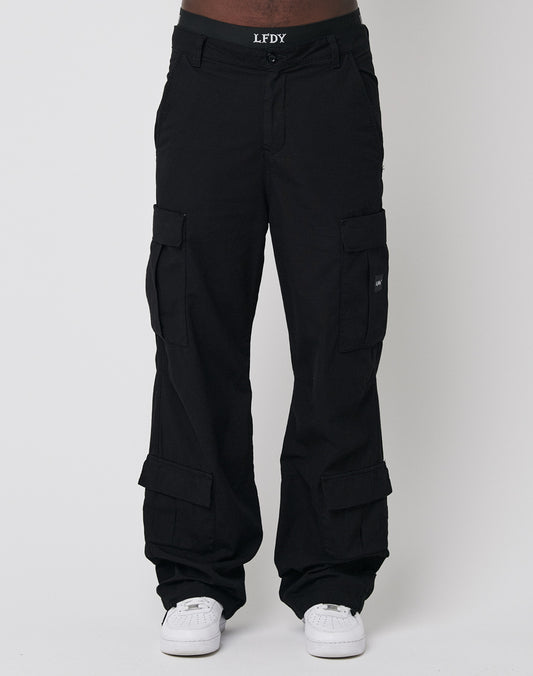 A person wears LFDY’s Wide Summer Cargo—black, wide fit cotton pants with multiple pockets—styled with a branded LFDY belt and white sneakers, standing against a plain light background.