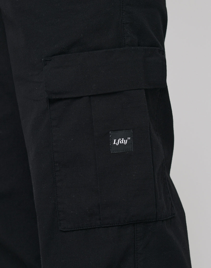 Close-up of a black LFDY Wide Summer Cargo pant leg in wide fit, showing a large flap pocket and a small black tag with “LFDY™” in white, made from premium Baumwolle.