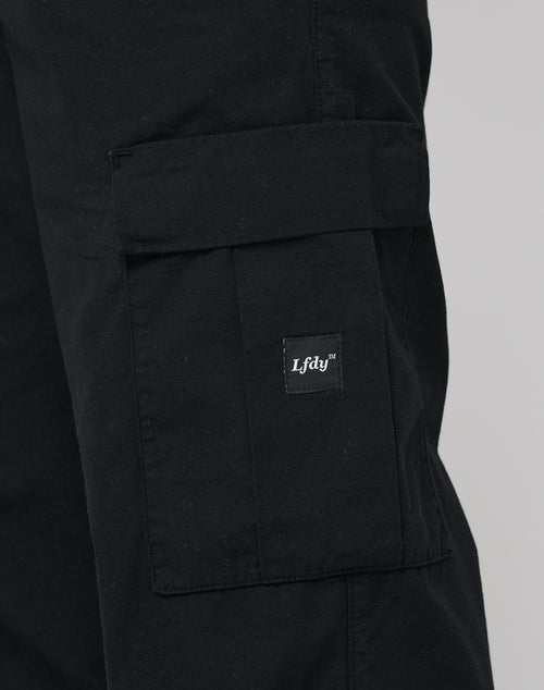 Close-up of a black LFDY Wide Summer Cargo pant leg in wide fit, showing a large flap pocket and a small black tag with “LFDY™” in white, made from premium Baumwolle.