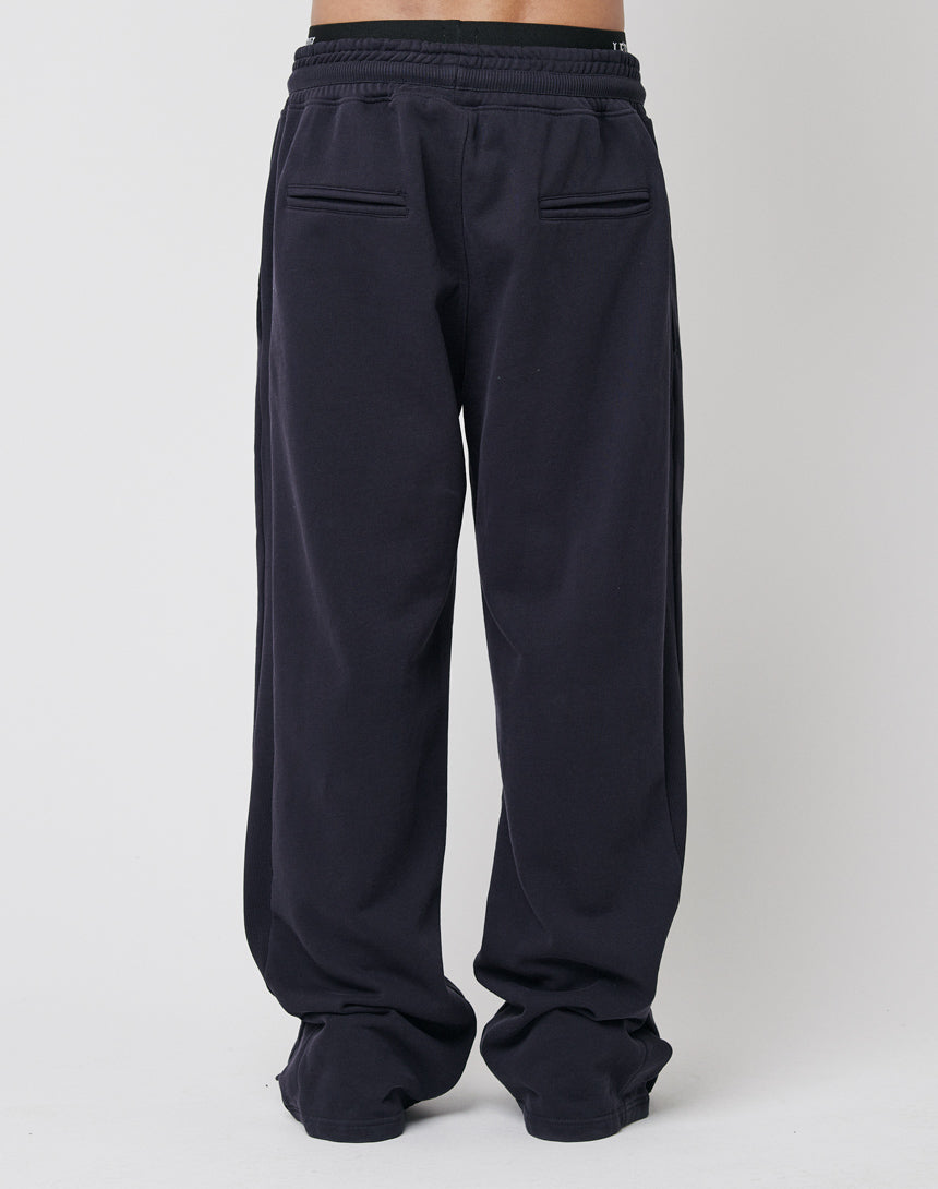 A person wears LFDY's Wide Jogger 2.0—loose-fitting, black joggers with a wide fit, elastic waistband, and two back welt pockets—standing against a plain light background, showing only their lower body.